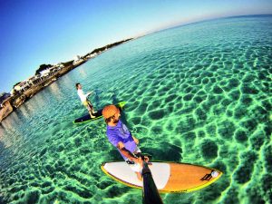 Paddler pe o placă de SUP navigând pe apele cristaline din Menorca. Experiență de neuitat de SUP în Menorca.